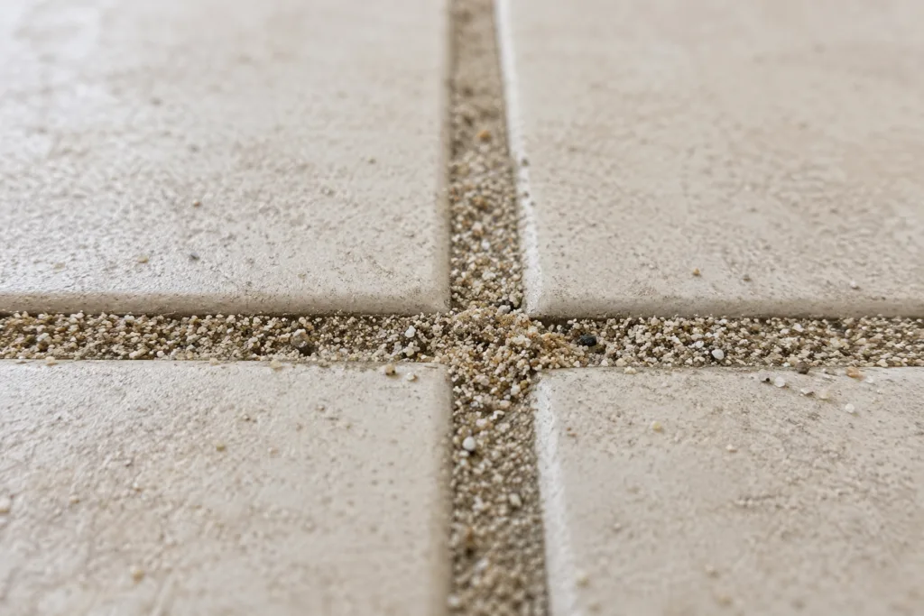 Close-up of sand embedded in balcony tile grout - the result of wet-over-dry cleaning without a prior vacuum step